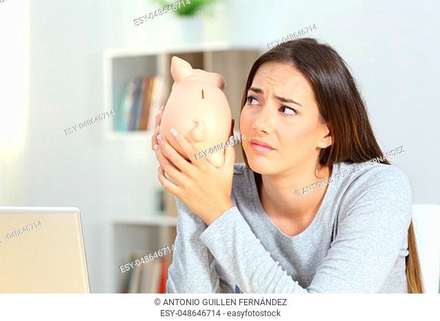 Sad woman shaking a piggy bank at home