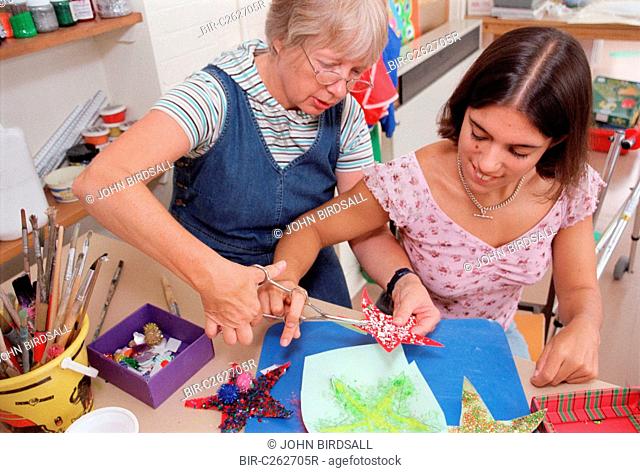 Carer assisting teenage girl to use dual control training scissors in residential respite care home