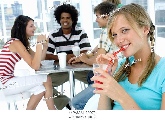 Portrait of a young woman drinking juice in a restaurant with her friends sitting in the background