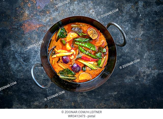 Traditional Thai kaeng phet red curry with vegetables as top view in a wok with copy space