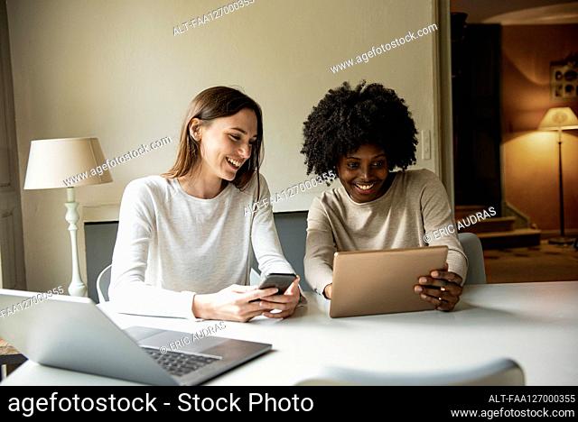 Smiling young women using digital tablet and smart phone at home