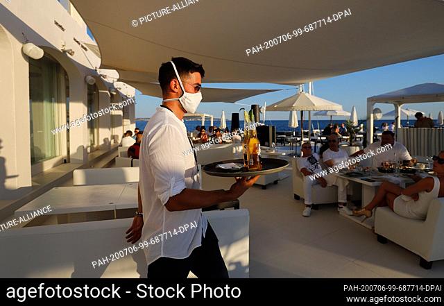 23 June 2020, Spain, Palma: A waiter with a face mask serves the customers of the Bar Purobeach in Cala Estancia on the beach Playa de Palma