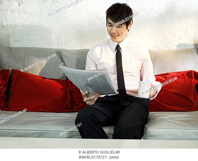 Asian businessman reading newspaper on sofa