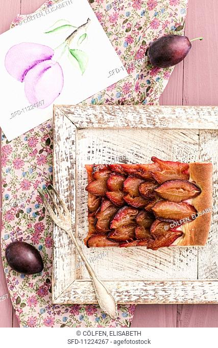 A slice of plum cake on a wooden tray and a picture of plums