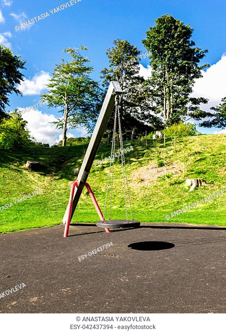 A swing with a rubber round seat hanging on four chains in Duthie park playground, Aberdeen, Scotland