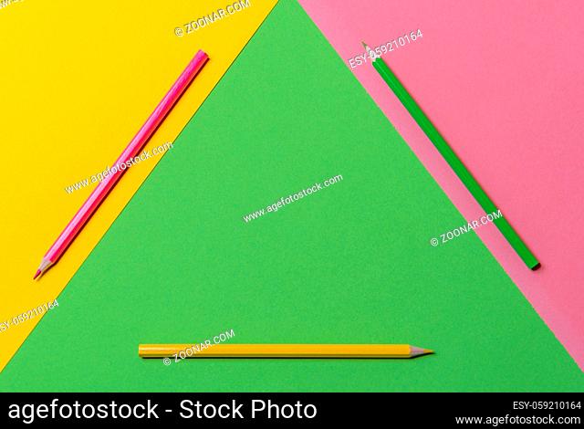 Desk in three colors with wooden pencils in green, yellow and pink, geometric displayed in a triangle. Above view with copy space. Back to school