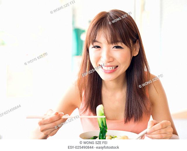 Asian girl eating vegetable noodles at Chinese restaurant. Young woman living lifestyle