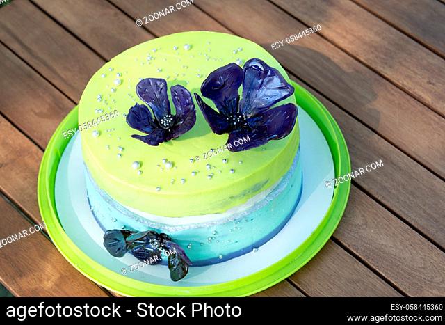 Birthday cake with blue edible flowers on wooden table at the garden