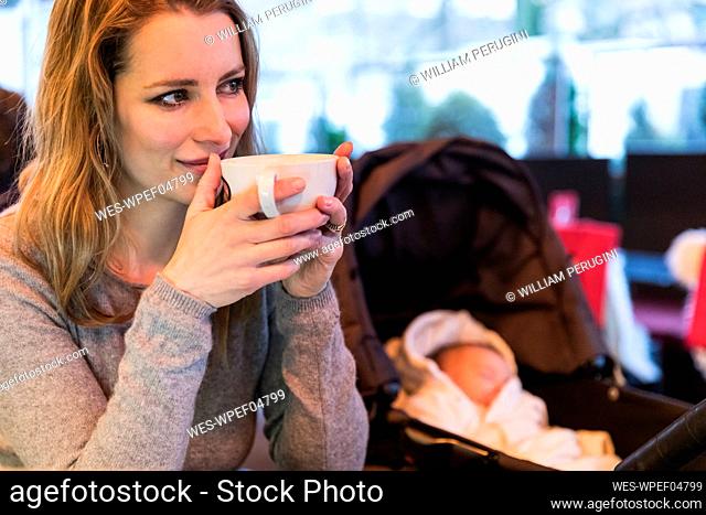 Smiling woman drinking coffee with baby in carriage in cafe