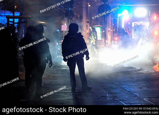 01 December 2023, Saxony, Leipzig: Police officers stand in front of the remains of burning garbage containers at Connewitzer Kreuz