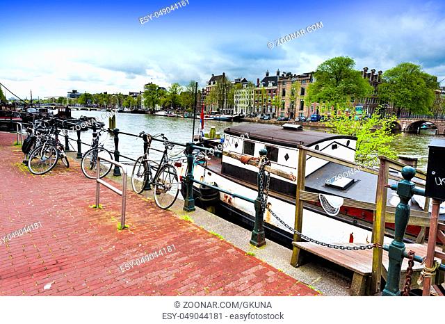 Urban scene in Amsterdam with houseboat and many bicycles. Street View with bikes parked on an embankment in the historical center of Amsterdam in the...