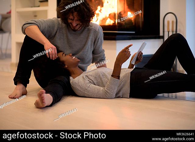 beautiful young multiethnic couple using tablet computer on the floor of their luxury home in front of fireplace at autumn day