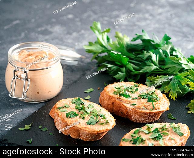 Close up view of slice bread with homemade turkey pate and fresh green parsley on black slate board over gray concrete background, Copy space