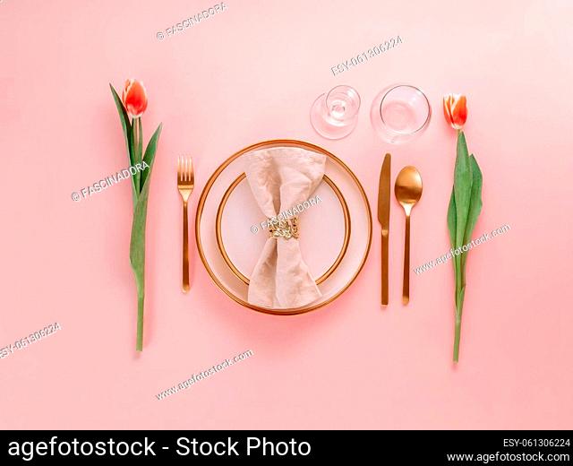 Festive pink table setting. Pink plate with gold cutlery and red tulip on pink background. Aesthetic stylish dinner table setting for Women's day, Mother's Day