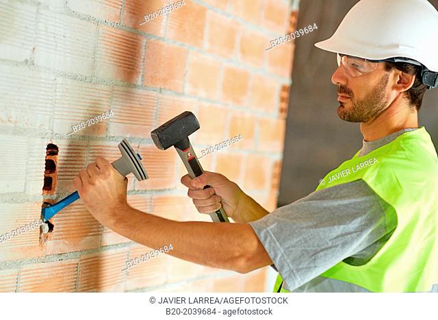 Bricklayer making a groove in the brick wall to place electrical wires. Hammer and chisel hand tools. Construction. Building work. Donostia