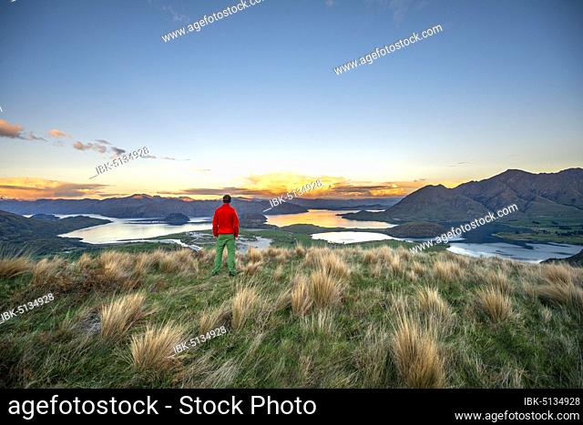 Walker looks out over Wanaka Lake and mountains at sunset, Rocky Peak, Glendhu Bay, Otago, South Island