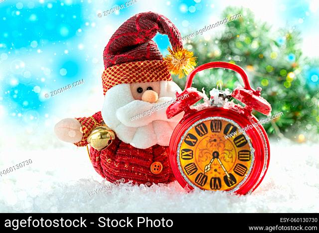 Christmas card with Santa Claus and red alarm clock in the snow on the background of a Christmas tree with lights. Christmas concept with copy space