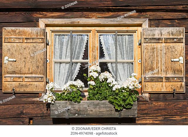 Fenster mit Fensterläden und Blumenschmuck an alter Almhütte