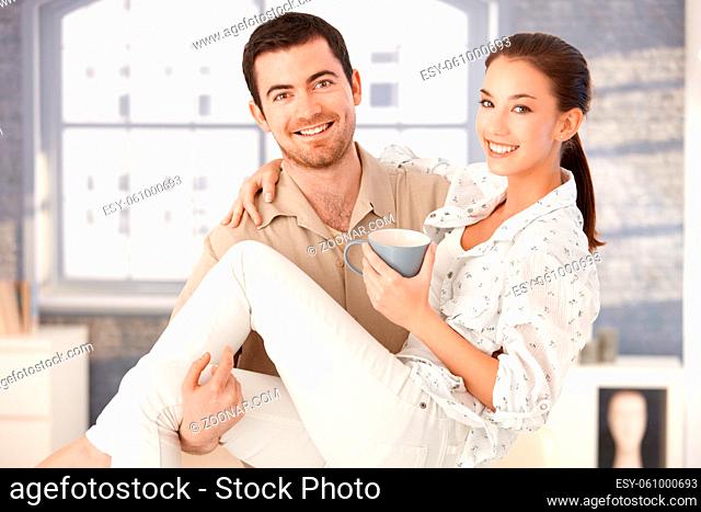 Happy young man holding woman in his arms, woman drinking tea, smiling