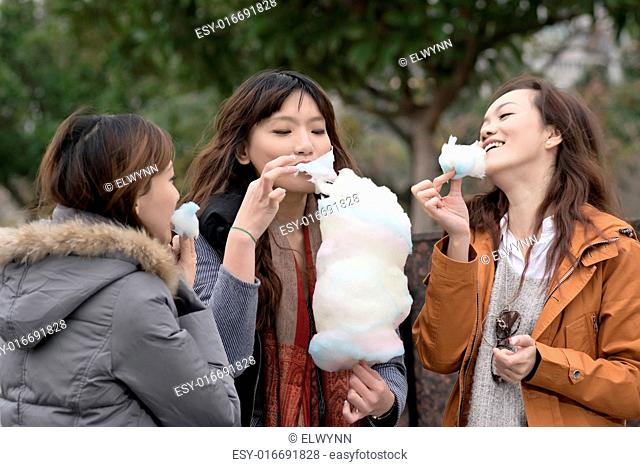 Happy young Asian woman eating cotton candy with her friends in outdoor