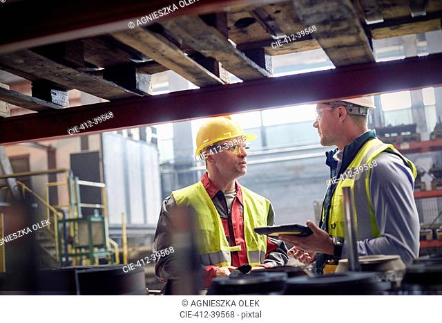 Steelworkers with digital tablet talking in steel mill