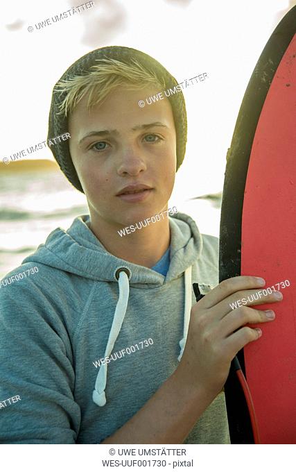 Portrait of teenage boy standing on the beach with his surfboard