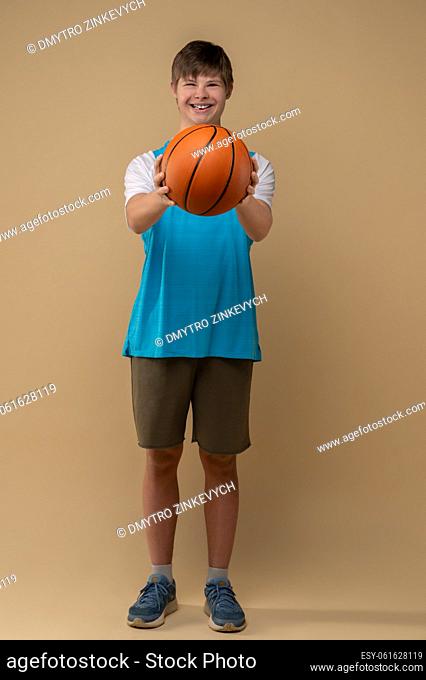 Full-length portrait of a joyful guy holding a round ball with both hands before him