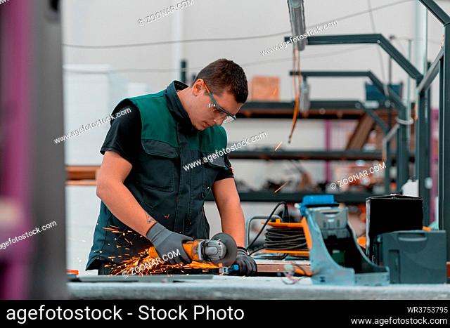 Heavy Industry Engineering Factory Interior with Industrial Worker Using Angle Grinder and Cutting a Metal Tube. Contractor in Safety Uniform and Hard Hat...