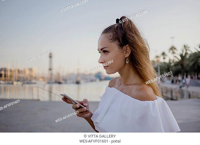 Young woman using smartphone at the harbour of Barcelona, portrait