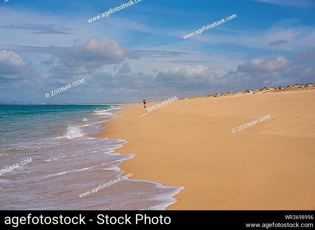 Fisherman fishing on a Comporta empty beach with ocean waves on the sand in Portugal