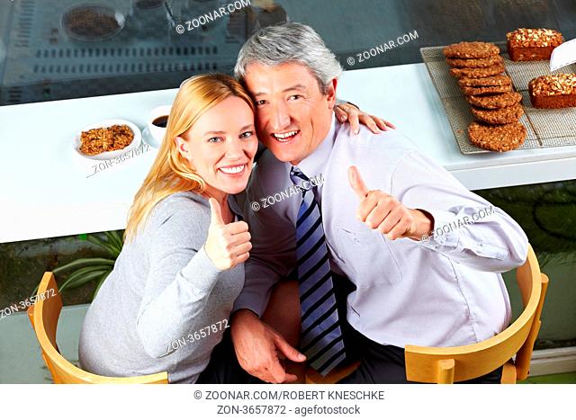 Älteres glückliches Paar im Café hält gemeinsam die Daumen hoch