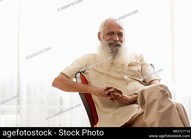A HAPPY OLD MAN SITTING AND POSING IN FRONT OF CAMERA