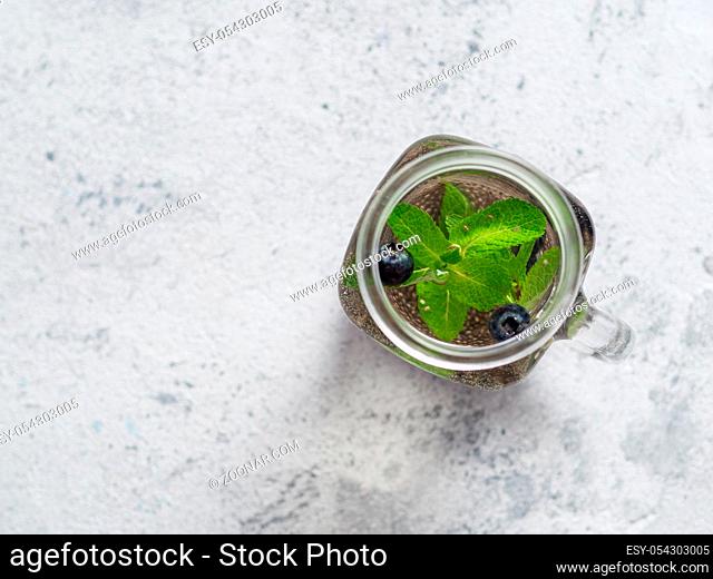 View from above chia water in mason jar with mint and blueberry on gray cement background.Chia infused detox water with berries.Copy space for text