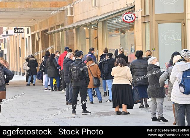24 March 2021, Bavaria, Munich: Passers-by wait for admission in Kaufinger Straße in front of a department store. Photo: Peter Kneffel/dpa