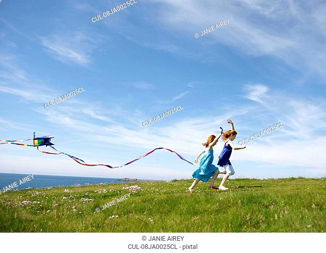 2 girls running with kites in field
