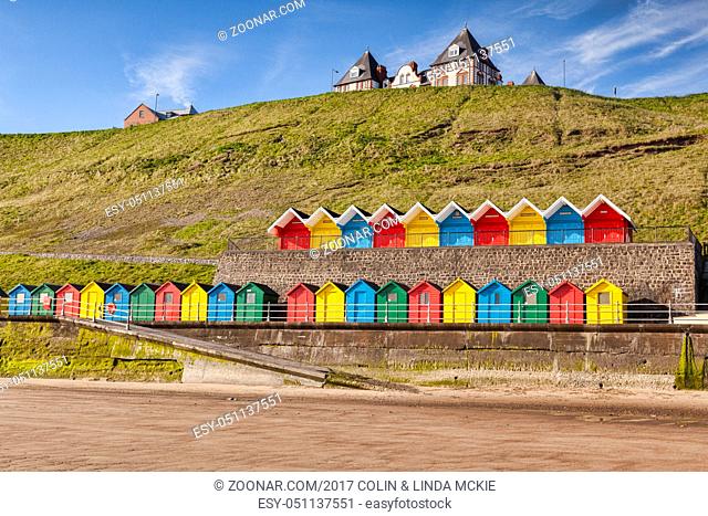 Rows of colorful beach huts on the promenade at Whitby Sands, Whitby, North Yorkshire, England, UK, on a beautiful sunny morning in spring