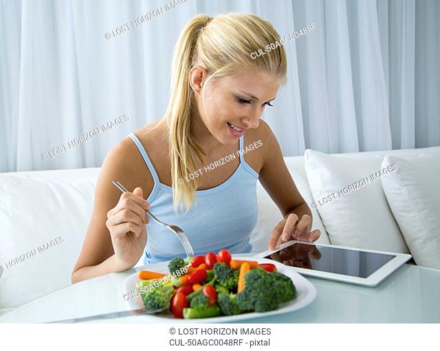 Woman using tablet computer and eating
