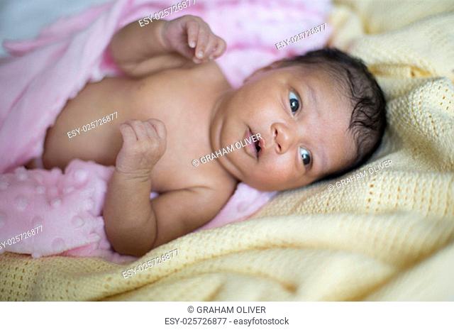 A beautiful newborn mixed race baby girl lying down wrapped in a pink blanket