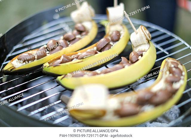 23 August 2019, Saxony, Leipzig: Bananas with chocolate sweets lie on a grill in a park in Leipzig during a barbecue party