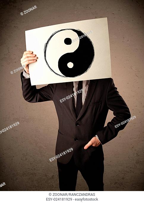 Businessman holding a paper with a yin-yang on it in front of his head