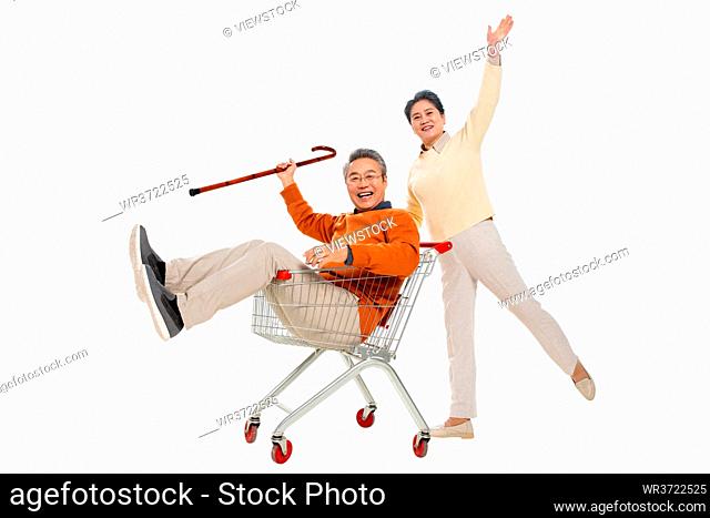 A happy old man pushes his wife sat in the shopping cart