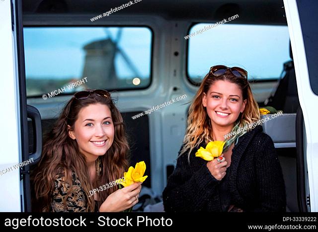 Two young women sit in a vehicle holiday fresh-picked yellow tulips. A journey outside of Amsterdam central leads to the coastal city of Egmond aan Zee