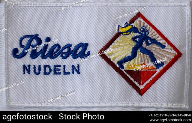 18 December 2023, Saxony, Riesa: The Minister President of Saxony wears a smock with the pasta manufacturer's logo at the inauguration of a new production...