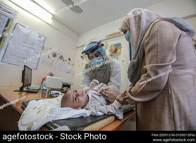 13 September 2020, Palestinian Territories, Gaza: A Palestinian health worker wearing a face mask gives polio vaccine to a child at a clinic run by the United...