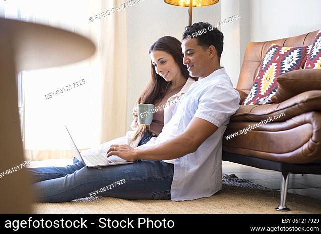 Young boy and girl together at home enjoying laptop computer sitting on the floor smiling and laughing - new life married people in love and relationship have...