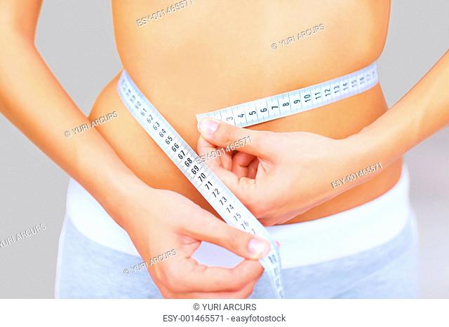 Cropped image of caucasian woman measuring her waistline with a measuring tape