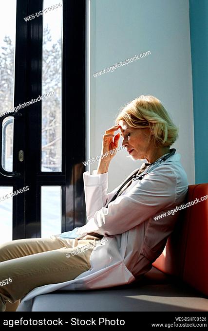 Tired mature doctor with head in hand sitting on couch in clinic