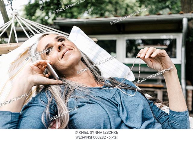 Smiling woman on the phone lying in hammock in the garden