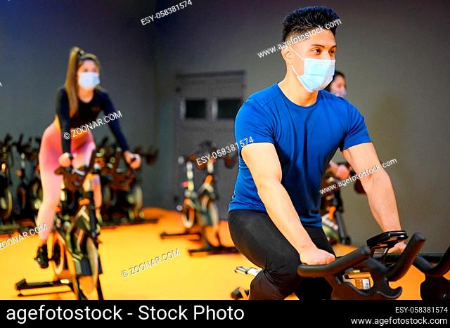 Young People Spinning in the fitness gym with protective face mask during coronavirus outbreak . High quality photo
