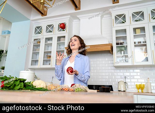 Happy woman juggling with apples in kitchen at home